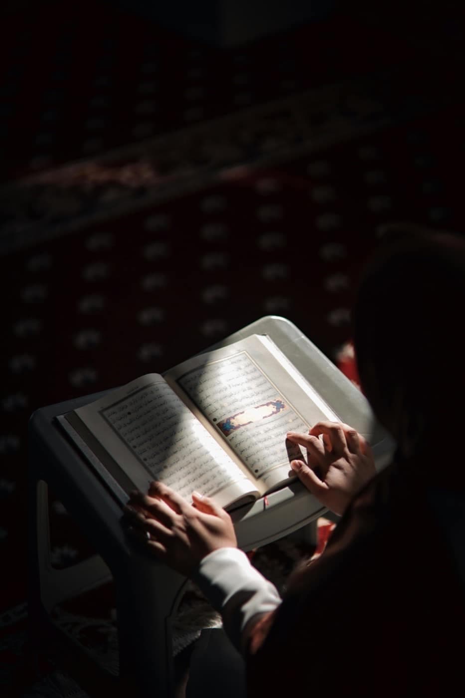 طالبة تقرأ القرآن من مصحف على حامل في ضوء هادئ